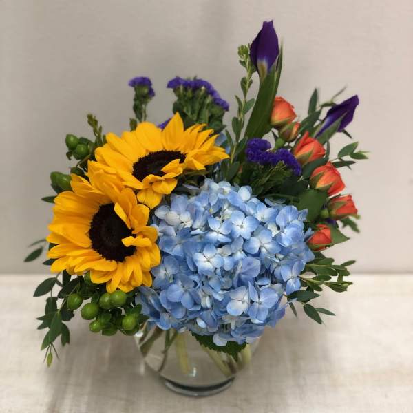 Bouquet of sunflowers, blue hydrangea, and orange roses in a glass vase