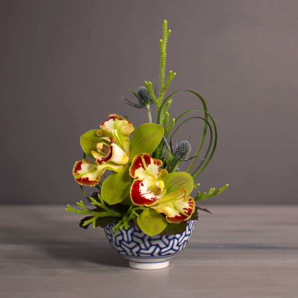 Small floral arrangement in a blue-and-white patterned bowl with yellow-red orchids