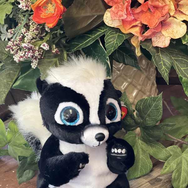 Plush skunk toy sitting in front of an artificial floral arrangement