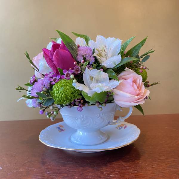 Mixed pink, white, and green flowers arranged in a white teacup on a saucer