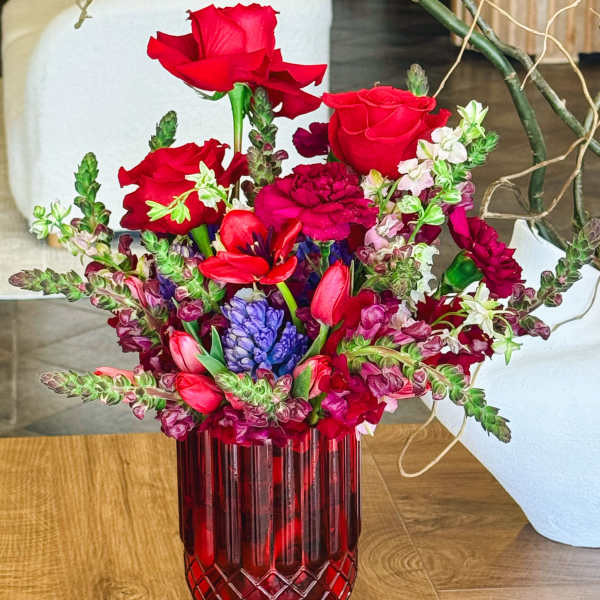 Red roses and mixed blooms arranged in a red glass vase