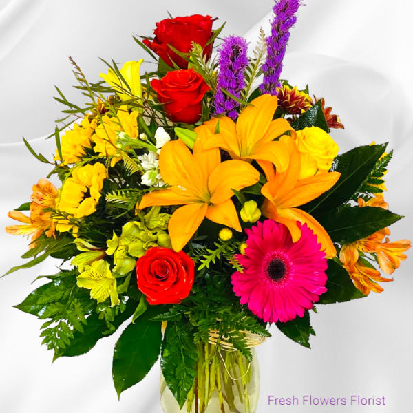 Mixed bouquet of roses, lilies, and gerbera daisies in a glass vase