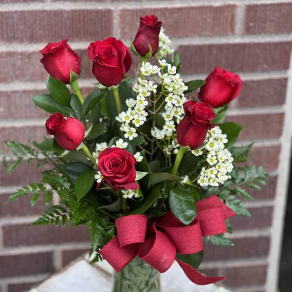 Red roses with white filler flowers in a glass vase and red ribbon