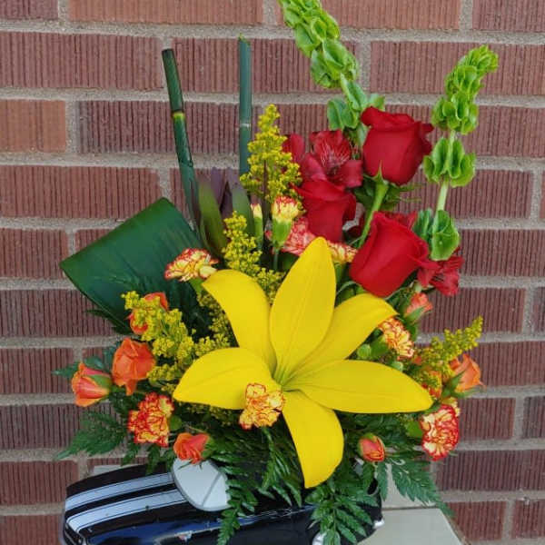 Floral arrangement in a toy car with red roses and a large yellow lily