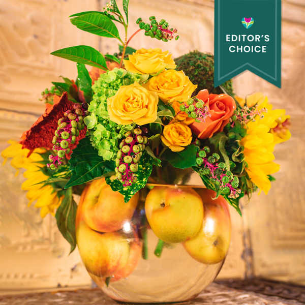 Bouquet of yellow and orange roses in a glass vase with apples