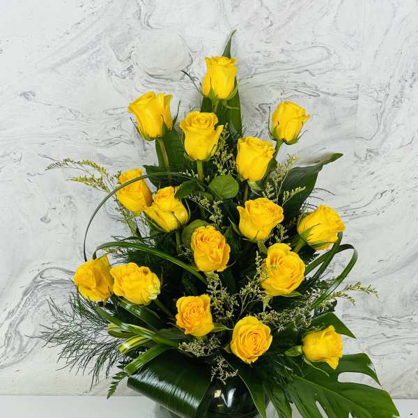 Yellow roses arranged in a glass vase with dark green foliage.