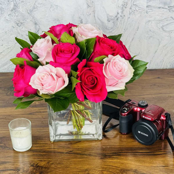 Pink and red roses in a square glass vase on a wooden table