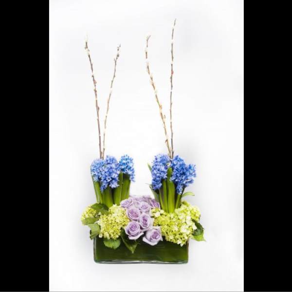 Blue and lavender flowers arranged in a rectangular vase with tall branches