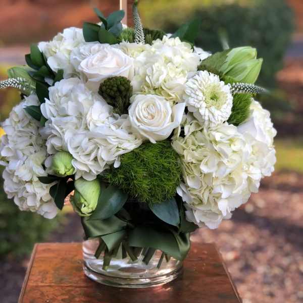 White floral arrangement in a clear glass vase with green accents