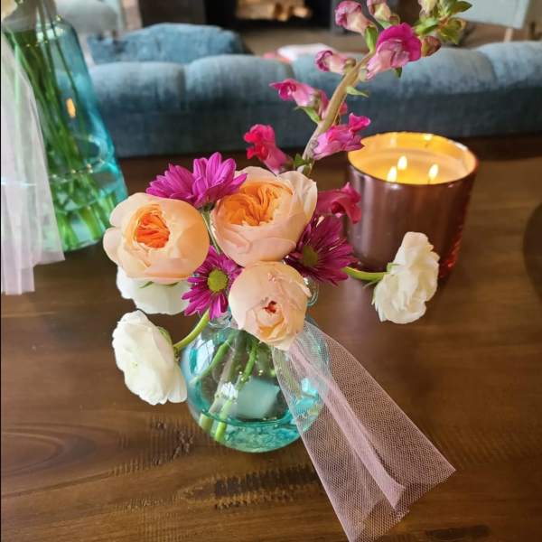 Small bouquet of peach and purple flowers in a blue glass vase with pink tulle