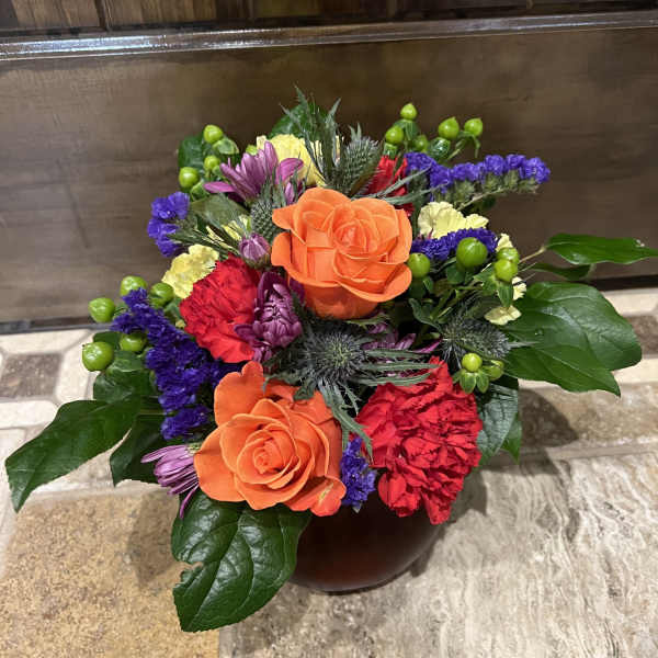 Colorful bouquet with orange roses and purple, red, and yellow flowers in a vase