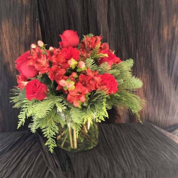 Red rose bouquet in a clear glass vase with evergreen foliage