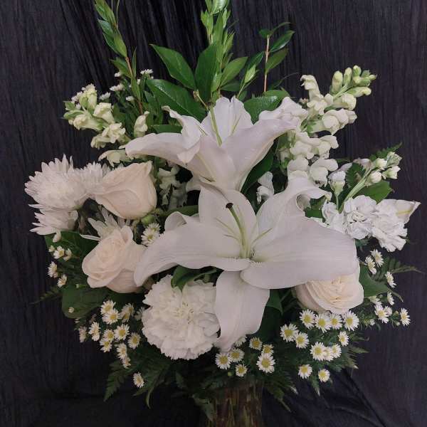 White lilies and roses arranged in a tall vase with greenery