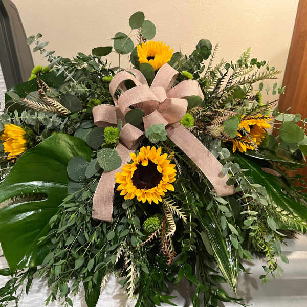 Large floral spray with sunflowers, greenery, and a pink ribbon bow