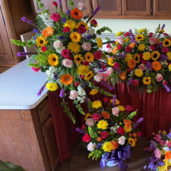 Set of bright mixed funeral sprays and a casket spray with yellow, pink, orange, and purple flowers.