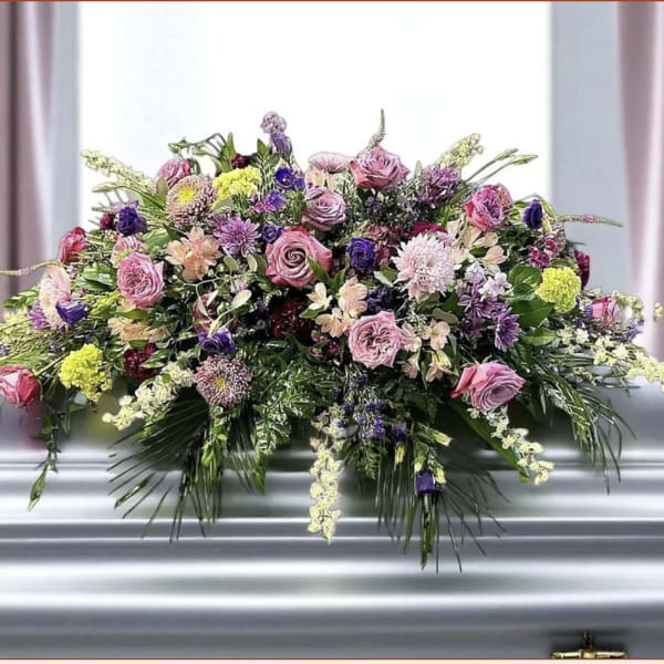 Large pink and purple floral casket spray on a silver casket