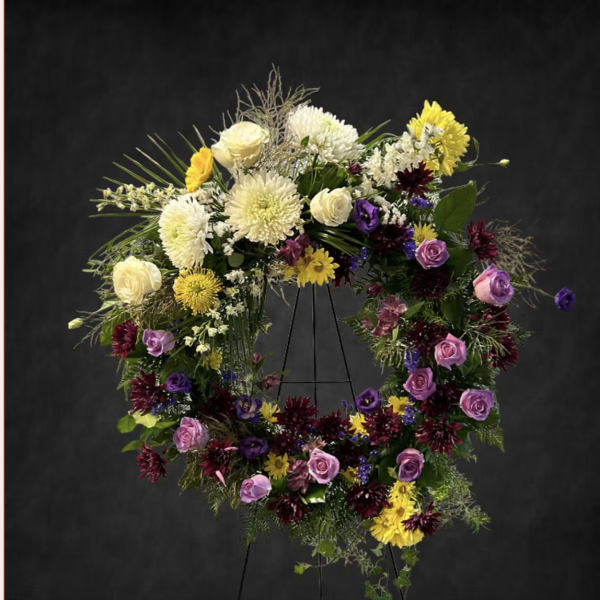 Large floral wreath on a stand with purple, yellow, and white blooms
