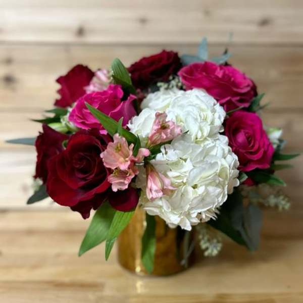 Bouquet of red and pink roses with white hydrangeas in a gold vase
