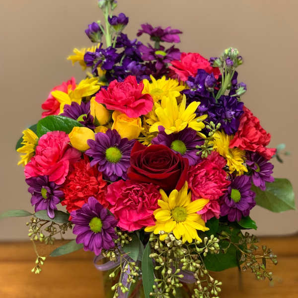 Colorful bouquet of daisies, carnations, and a red rose in a glass vase