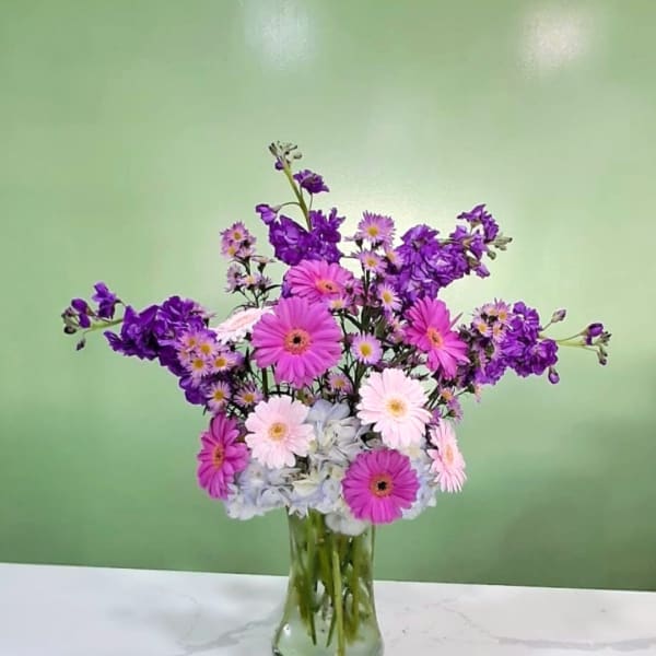 Pink and purple daisy bouquet in a clear glass vase