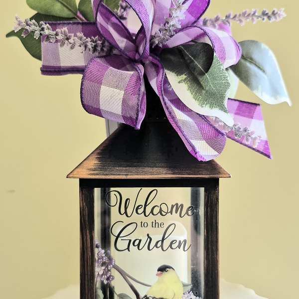Decorative lantern with a purple ribbon bow and faux greenery