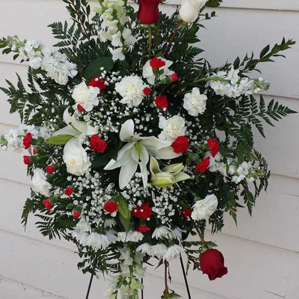 Standing funeral spray with red and white flowers on a black easel