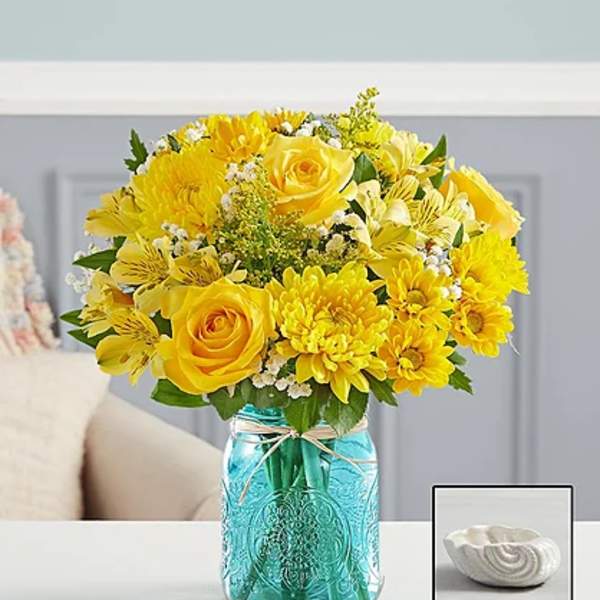 Yellow bouquet in a blue glass mason jar with a small white dish beside it