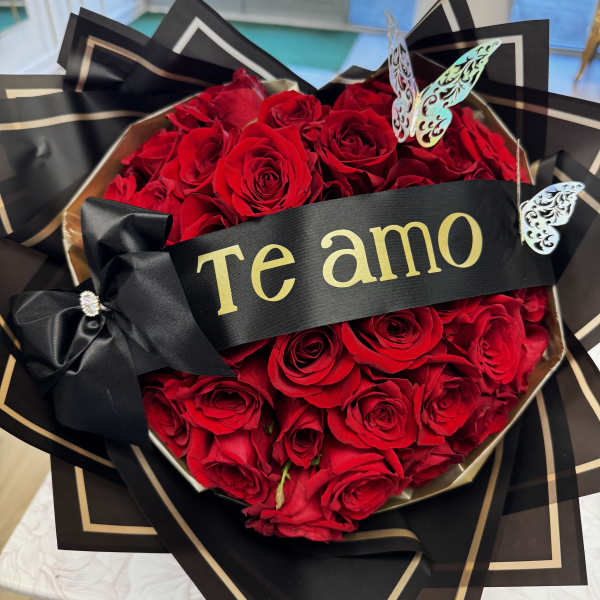 Heart-shaped bouquet of red roses with a black ribbon and "Te amo" banner