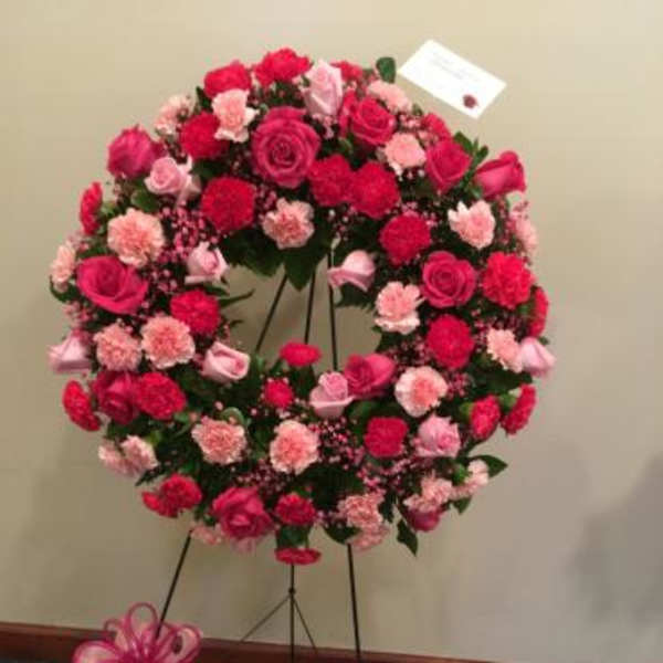 Pink and red floral wreath on a stand with ribbon bows