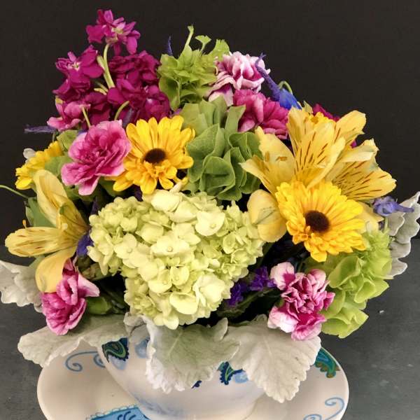 Colorful mixed flower arrangement in a white teacup on a patterned saucer