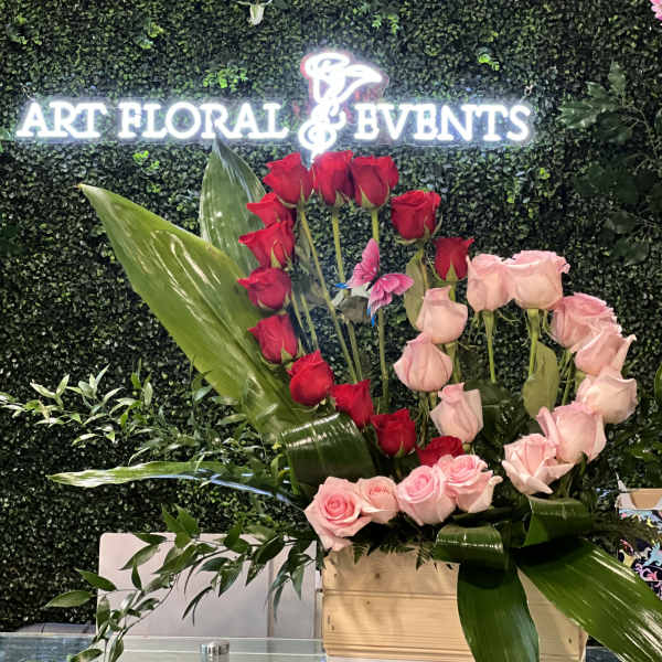 Red and pink roses arranged in a wooden box with large tropical leaves