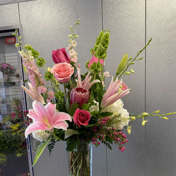 Tall mixed bouquet of pink lilies, roses, and protea in a glass vase