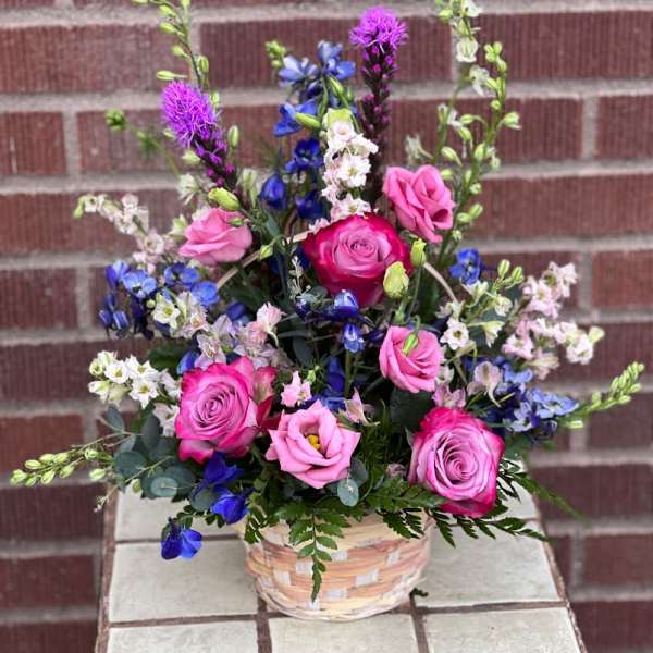 Mixed pink and blue flower arrangement in a woven basket