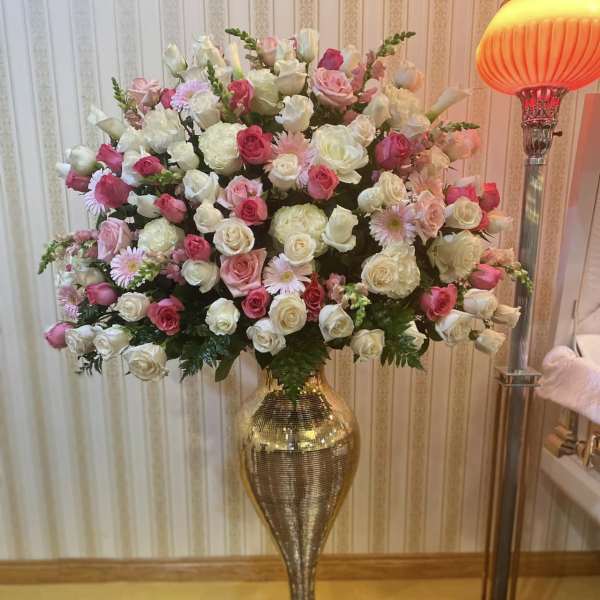 Large pink and white rose arrangement in a tall gold vase