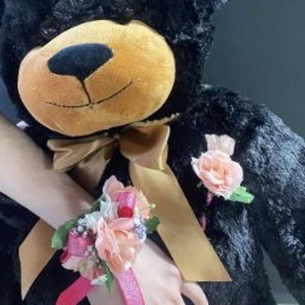 Black teddy bear with a gold bow and pink floral wrist corsage