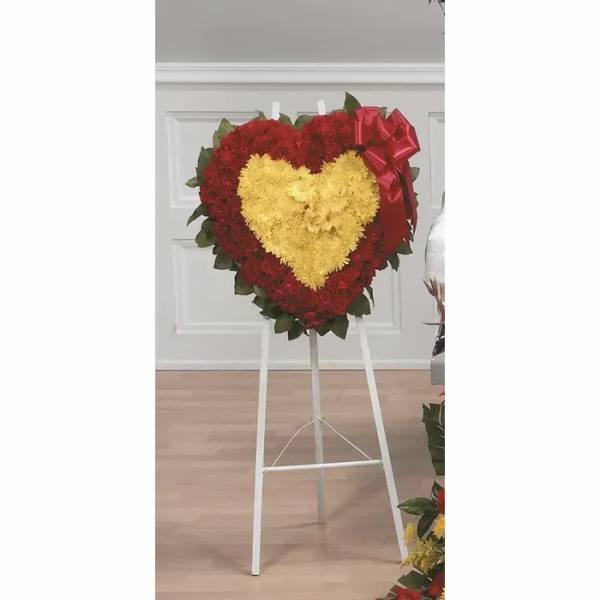 Heart-shaped floral wreath on a stand with red and yellow flowers and a red bow