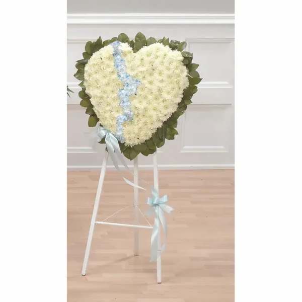 Heart-shaped white floral wreath on a stand with a blue ribbon