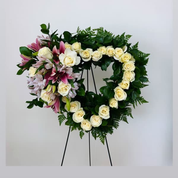 Heart-shaped floral wreath of white roses and pink lilies on a stand
