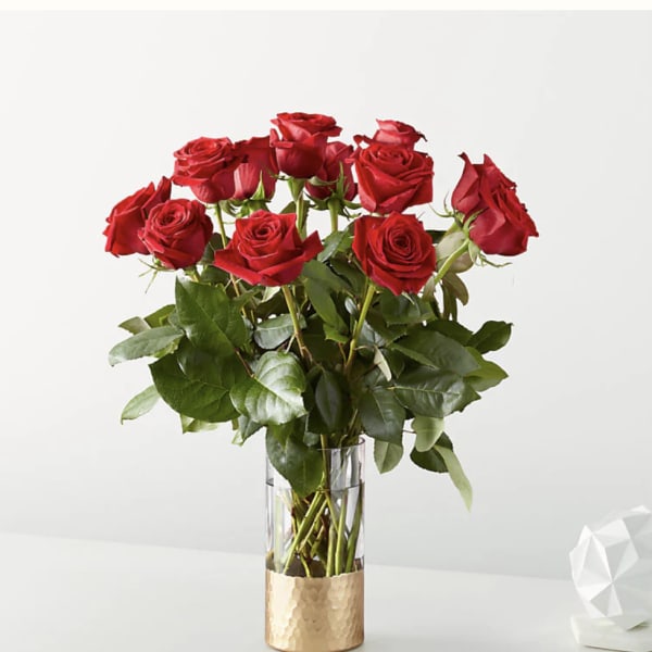 Tall arrangement of red roses in a clear glass vase with a gold base