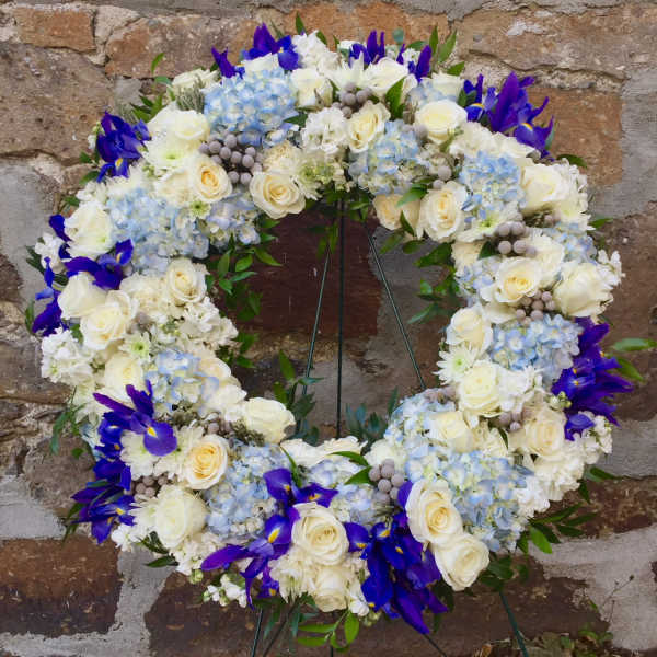 Circular floral wreath with white roses, blue hydrangeas, and purple irises