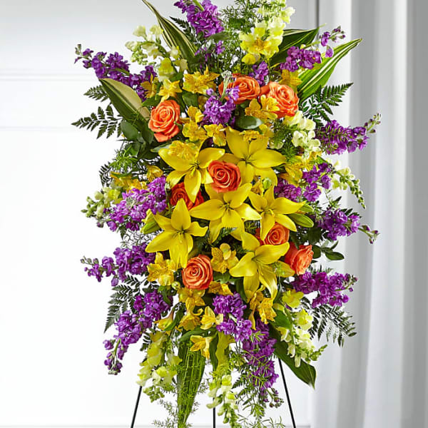 Tall standing floral spray with yellow lilies, orange roses, and purple flowers