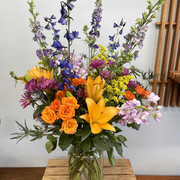 Colorful mixed bouquet in a clear glass vase with orange roses and yellow lilies