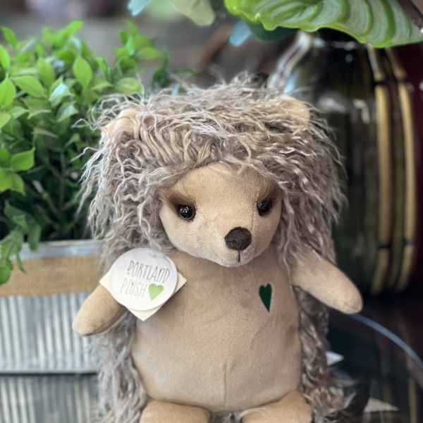 Plush hedgehog toy with a tag, displayed among potted flowers