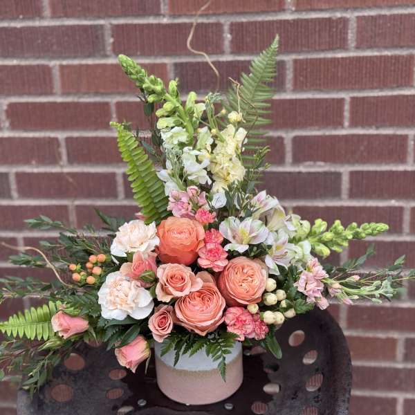 Peach and pink floral arrangement in a pink vase with fern accents