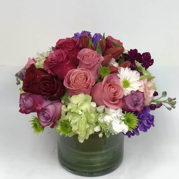 Mixed bouquet of roses, lilies, and daisies in a green glass vase