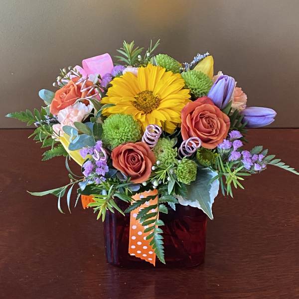 Mixed bouquet in a dark glass vase with yellow, orange, purple, and green flowers