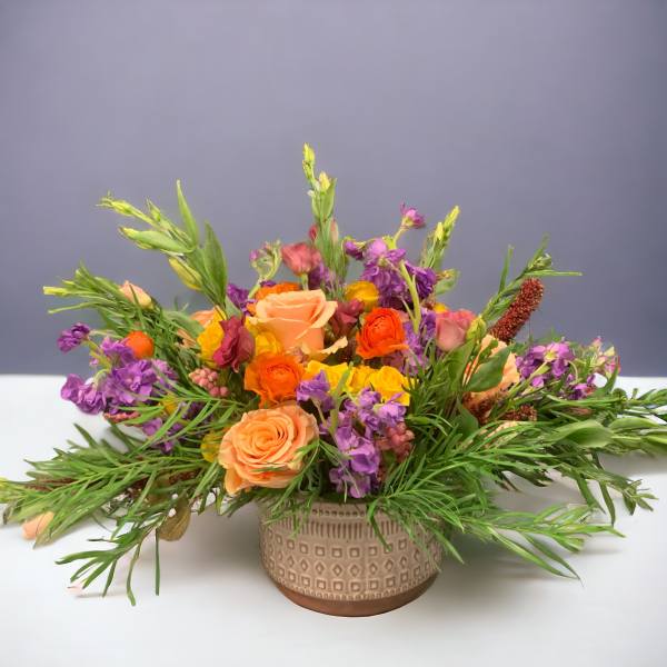 Mixed bouquet of peach, orange, yellow, and purple flowers in a patterned vase