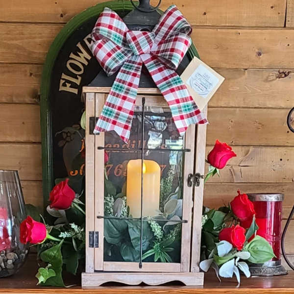 Lantern with candle, red roses, and plaid bow on a wooden shelf