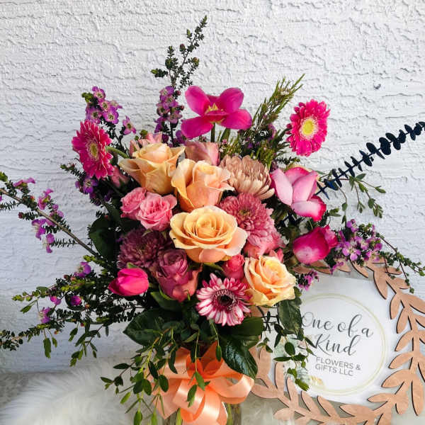 Mixed pink and peach flower bouquet in a glass vase with a ribbon