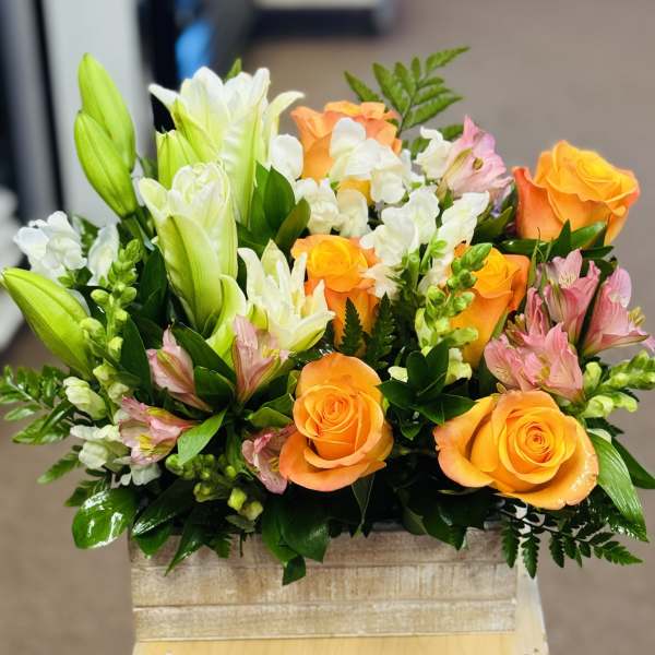 Mixed bouquet of orange roses, white lilies, and pink alstroemeria in a square container